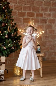 The adorable little girl in gorgeous dress standing near Christmas tree.