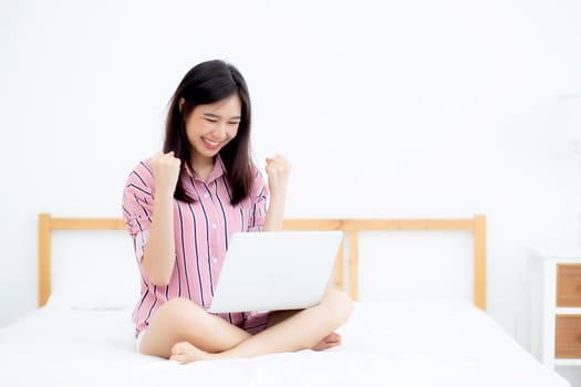 Beautiful of portrait asian young woman sitting relax and leisure with laptop internet online on vacation in bedroom, cheerful of asia girl with gesture glad and success, lifestyle concept.