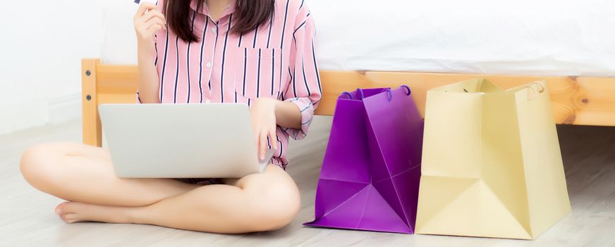 Banner website beautiful asian woman shopping online with laptop computer sitting on floor on room, girl holding credit card purchase and shopping bags, lifestyle concept.
