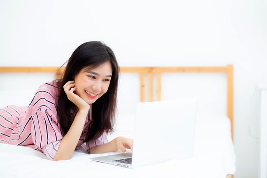 Beautiful asian young woman lying on bed using laptop at bedroom for leisure and relax, freelance with girl working notebook, communication concept.