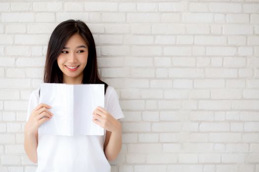 Beautiful of portrait young asian woman happiness relax standing reading book on concrete cement white background at home, girl happy study content literature, education and lifestyle concept.