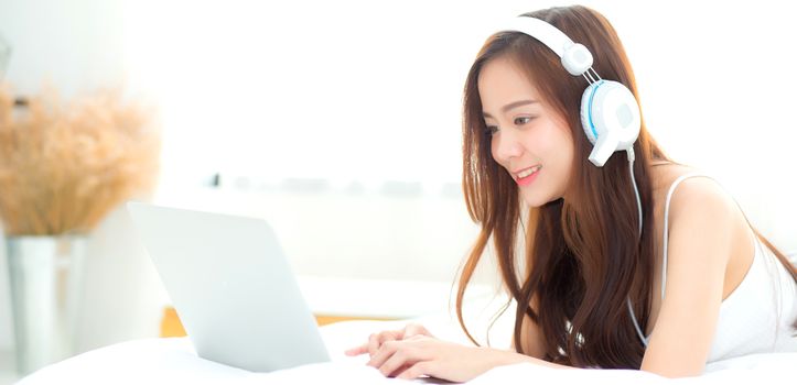 Banner website beautiful asian young woman relax listening to music with headphone and laptop online internet on vacation in bedroom, cheerful of asia girl leisure, lifestyle concept.