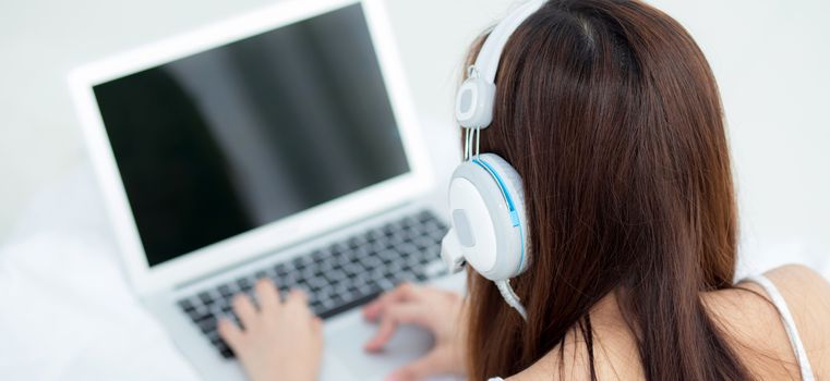 Banner website beautiful asian young woman relax listening to music with headphone and laptop online internet on vacation in bedroom, cheerful of asia girl leisure, top view, lifestyle concept.