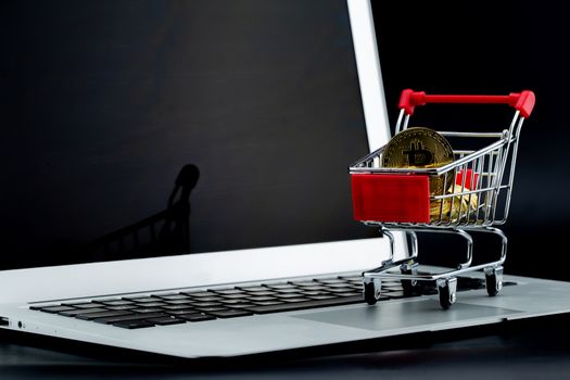 Shopping carts with gold bitcoin on laptop computer isolated on black background, digital currency money trading with cryptocurrency, coin with profit, finance concept.