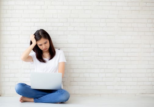 Beautiful of portrait asian young woman working online laptop and thinking and serious sitting on floor brick cement background, freelance girl using notebook computer, business and lifestyle concept.