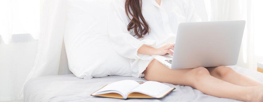 Banner website beautiful asian young woman setting on bed using laptop computer and notebook at bedroom for leisure and relax, freelance with girl working at bedroom with note, communication and lifestyle concept.