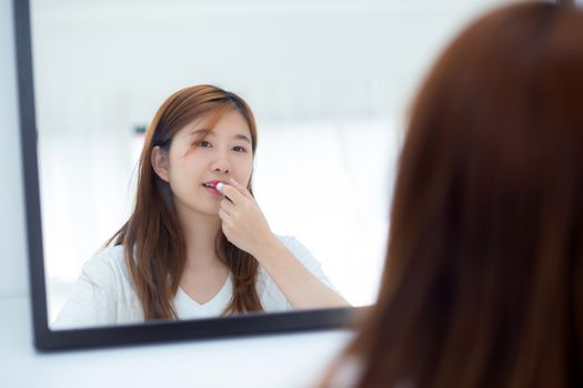 Beauty of portrait of young asian woman at the mirror holding and looking a makeup lipstick, Beautiful girl beauty fashion at the room, lifestyle concept.