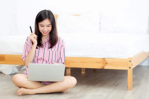 Beautiful of portrait young asian woman sitting users credit card with laptop, content girl shopping online and payment with notebook computer on bed at bedroom, lifestyle concept.