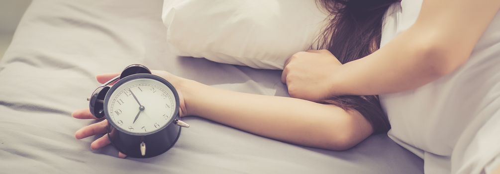Banner website closeup asian young woman turn off alarm clock in good morning, wake up for sleep with  girl holding alarm clock, time and lifestyle concept.