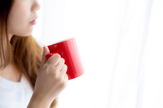 Beautiful of portrait young asian woman with drink acup of coffee standing curtain window background in bedroom, girl relax in morning at home, lifestyle concept.