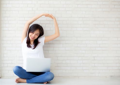 Beautiful portrait young asian woman sitting with laptop stretch and exercise relax after work success on cement concrete background, modern office with copy space, freelance business concept.