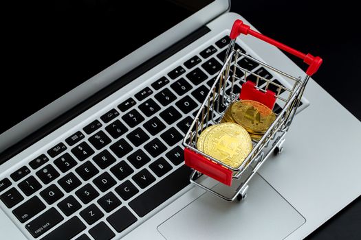 Shopping carts with gold bitcoin on laptop computer isolated on black background, digital currency money trading with cryptocurrency, coin with profit, finance concept, top view.
