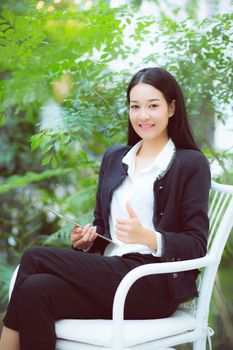 Beautiful portrait business young asian woman smile and happy sitting using digital tablet computer work at home, businesswoman on chair gesture excellent sign, communication concept.