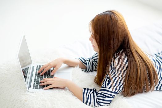 Beautiful asian young woman lying on bed using laptop at bedroom for leisure and relax, freelance with girl working notebook, communication concept.