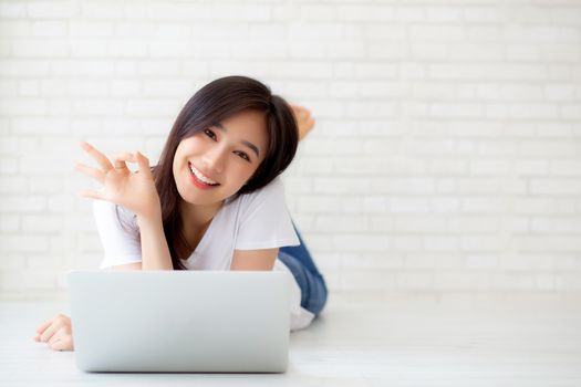 Beautiful portrait asian young woman working online laptop with excited lying on floor brick cement background, freelance girl smile using notebook computer with happy, business and lifestyle concept.
