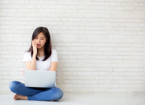 Beautiful of portrait asian young woman working online laptop and thinking and serious sitting on floor brick cement background, freelance girl using notebook computer, business and lifestyle concept.