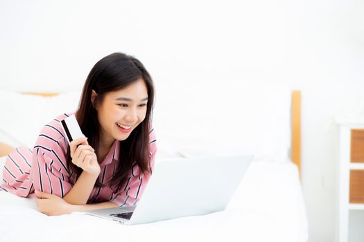 Beautiful of portrait young asian woman lying users credit card with laptop, content girl shopping online and payment with notebook computer on bed at bedroom, lifestyle concept.