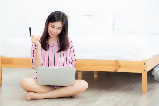 Beautiful of portrait young asian woman sitting users credit card with laptop, content girl shopping online and payment with notebook computer on bed at bedroom, lifestyle concept.