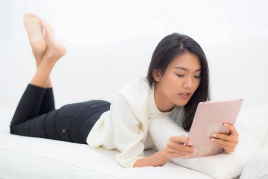 Beautiful portrait young asian woman smile and happy using digital tablet computer with lying couch at home, girl with satisfy social internet online, business communication concept.