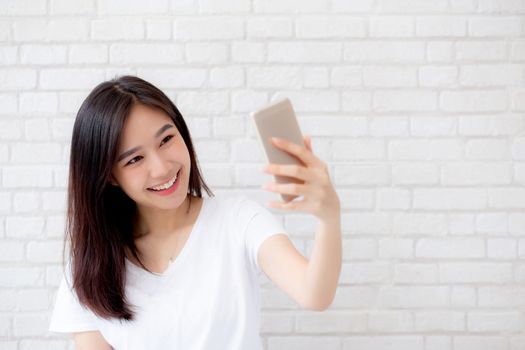 Beautiful portrait young asian woman taking a selfie with smart mobile phone on concrete cement white background, girl is photographing with happy and smile with fun, lifestyle concept.