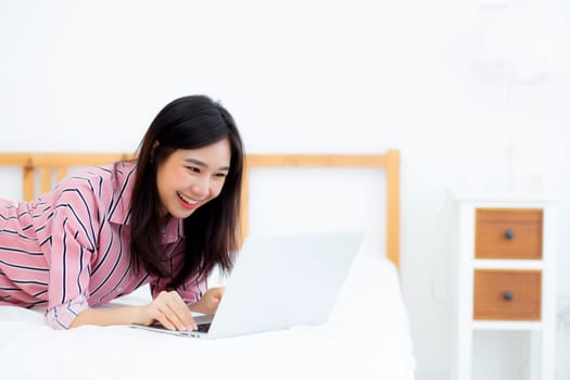 Beautiful asian young woman lying on bed using laptop at bedroom for leisure and relax, freelance with girl working notebook, communication concept.