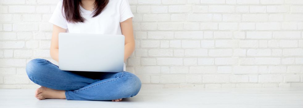 Banner website asian woman working online laptop sitting on floor brick cement background, freelance girl using notebook computer with connect to internet for distance job, business and lifestyle concept.