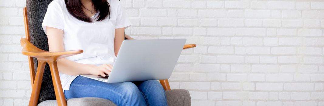 Banner website beautiful asian young woman working online laptop sitting on chair on cement brick white background, girl using notebook computer, business concept.