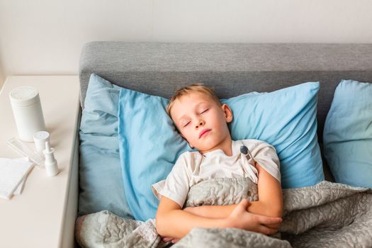 Sick little boy with high fever and headache laying in bed and holding thermometer. Stay at home during corona virus epidemic if you feel sick