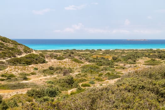 Landscape on the west coast of Rhodes island, Greece near Kattavia with green vegetation in the foreground and turqouise water in the background on a sunny day