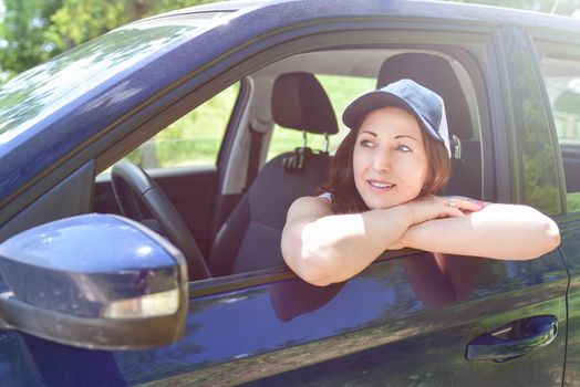 Smiling female driver in hat looking out the car. a portrait of a smiling woman sitting in the car, looking at the camera.