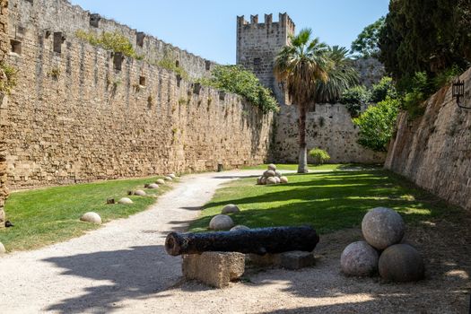 Along the ditch of the antique city wall in the old town of Rhodes city at greek island Rhodes on a sunny day in summer with canaonballs in the foreground