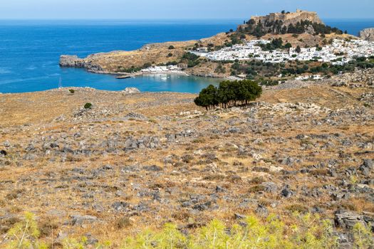 Scenic view at the city of Lindos with white houses, the antique Acropolis on top of the mountain and a bay on Rhodes island, Greece on a sunny day in spring