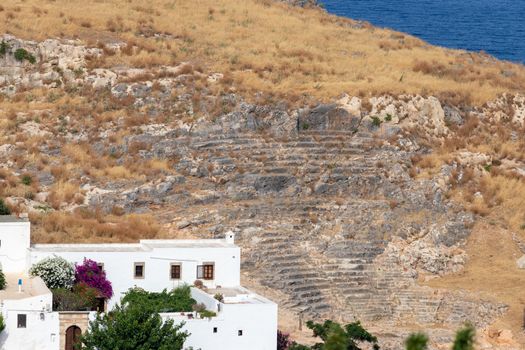 excavation of ancient amphitheater in Lindos on Greek island Rhodes with white house in foreground