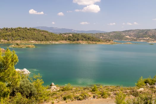 Scenic view at the Gadoura water reservoir on Rhodes island, Greece with blue and turquoise water and green landscape around the lake on a sunny day in spring