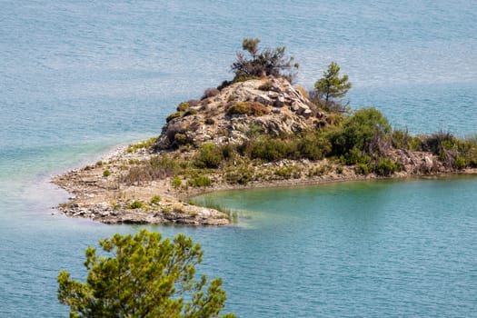 Small island of rocks and with green trees in the Gadoura water reservoir on Rhodes island, Greece on a sunny day in spring