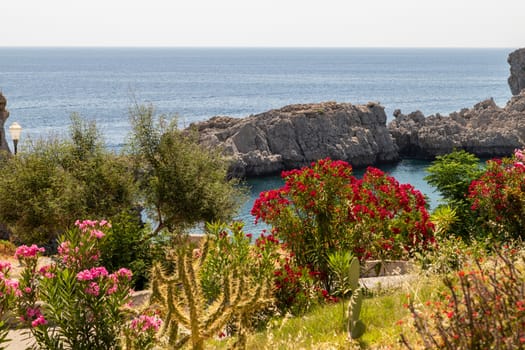 Scenic view at St. Pauls bay in Lindos on Rhodes island, Greece with red and purple flowers in the foreground  on a sunny day 