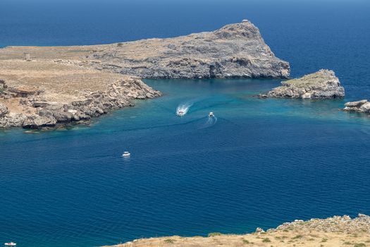 Coastline at Lindos on Greek island Rhodes with rocks in the water , motor boats and the mediterranean sea