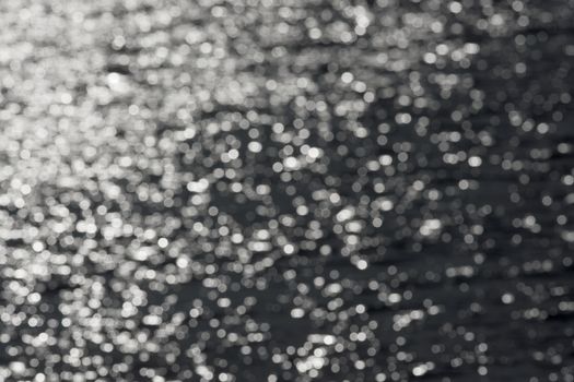 1 - Full frame sparkling out of focus spikes of light, formed from sunlight hitting ripples on a reservoir. monochrome dark grey against white.
