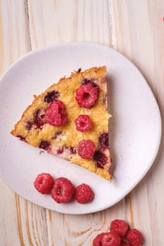 Sweet tasty pie slice with jellied and fresh raspberry fruits in plate, wooden table background, top view