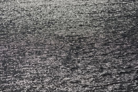1 - Full frame sunlight shining off surface ripples of large reservoir lake. Glittery shimmer effect. monochrome grey with bright sun flare spots.