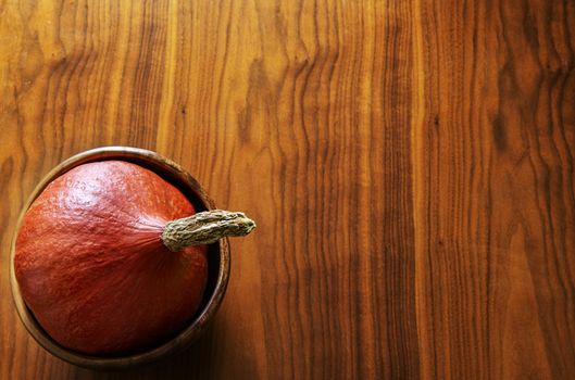 Orange pumpkin lying in a wooden bowl on a table