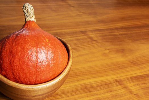 Orange pumpkin lying in a wooden bowl on a table