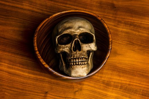 Scary halloween photo of a human skull lying in a wooden bowl on a table from the same wood