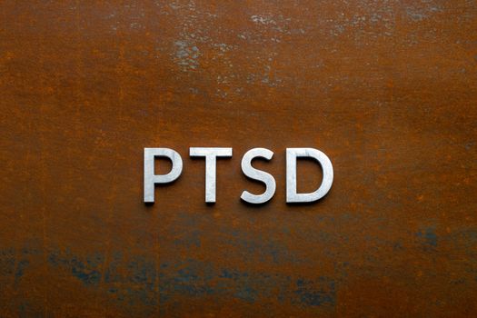 the word PTSD - post traumatic stress disorder - laid with silver metal letters on flat rusted sheet steel background in directly above perspective.