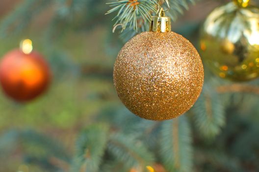 Christmas golden ball decoration ornament. Yellow holiday ball hanging from a green christmas tree twig. New year greeting card with copy space.