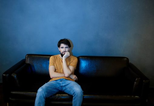 A man sits on a sofa indoors and watches TV front view. High quality photo