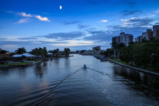 Boat returns to dock at dusk as the moon comes up over Wiggins Pass in Naples, Florida.