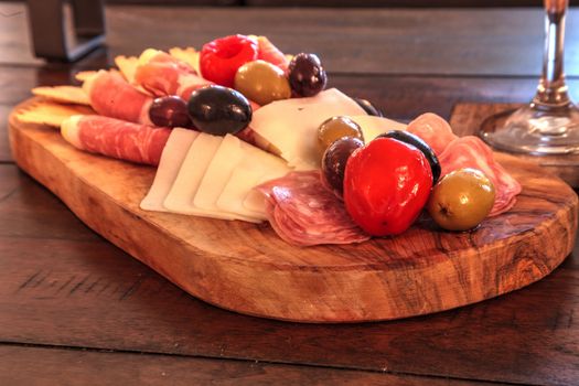 Charcuterie board on rustic wood with candles behind a spread of prosciutto, mozzarella cheese, Genoa salami, Fontina cheese and artisanal crackers.