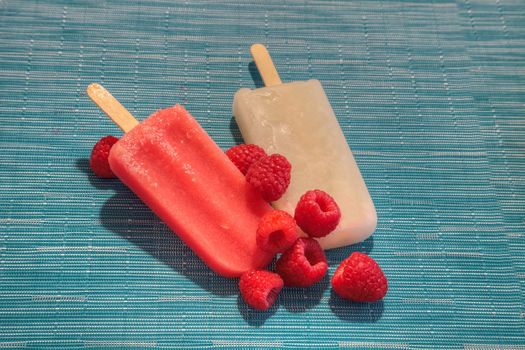 Fruit popsicles on an aqua blue background in summer including watermelon popsicle, tropical fruit popsicle, mango popsicle, and lime popsicle with fresh raspberries.