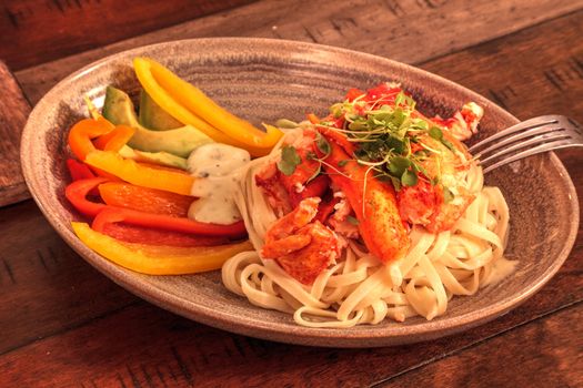 Maine lobster over a bed of linguini with micro greens, colorful peppers and avocado sauce.